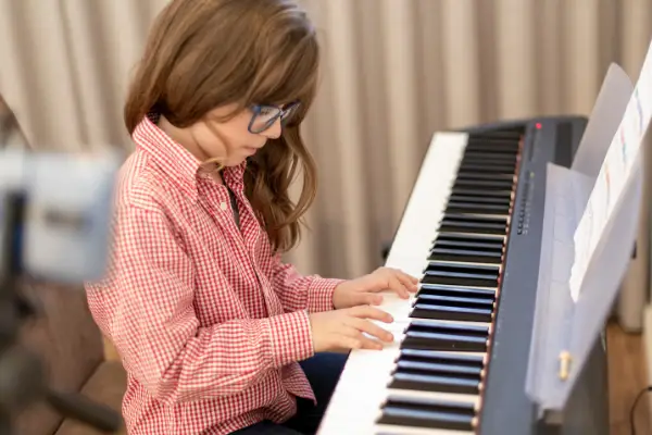 Young girl wearing glasses and red checked shirt Playing Music on a Piano Keyboard