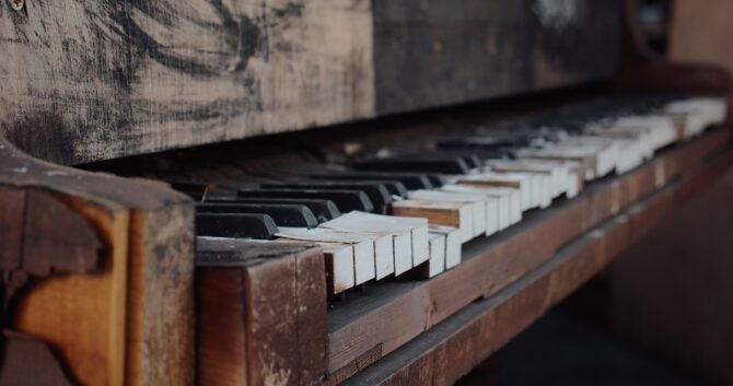Close-up image of an old, wooden piano with broken and uneven keys. 